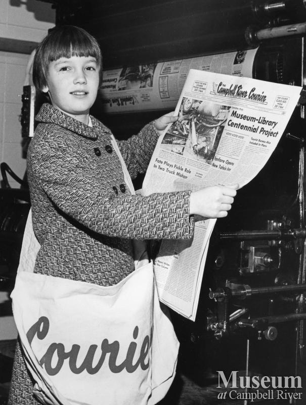 A young newspaper delivery girl holds front page of local newspaper