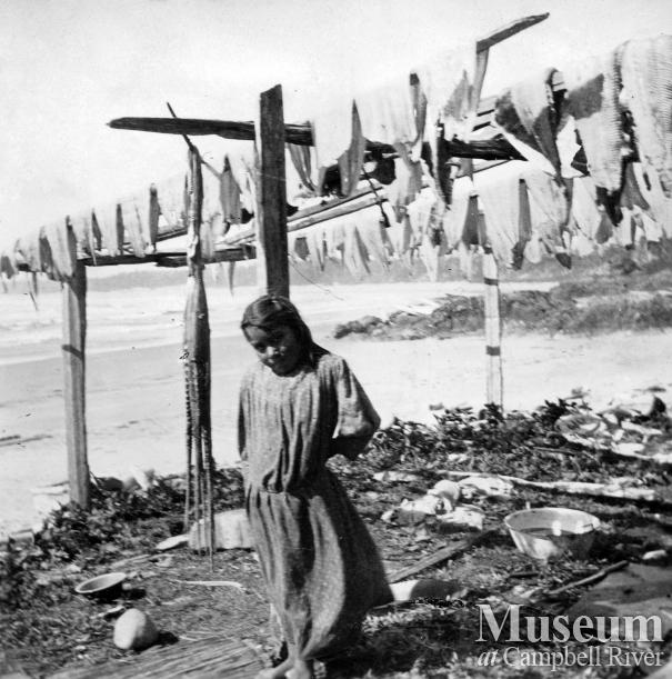 A young girl near some fish drying on waterfront